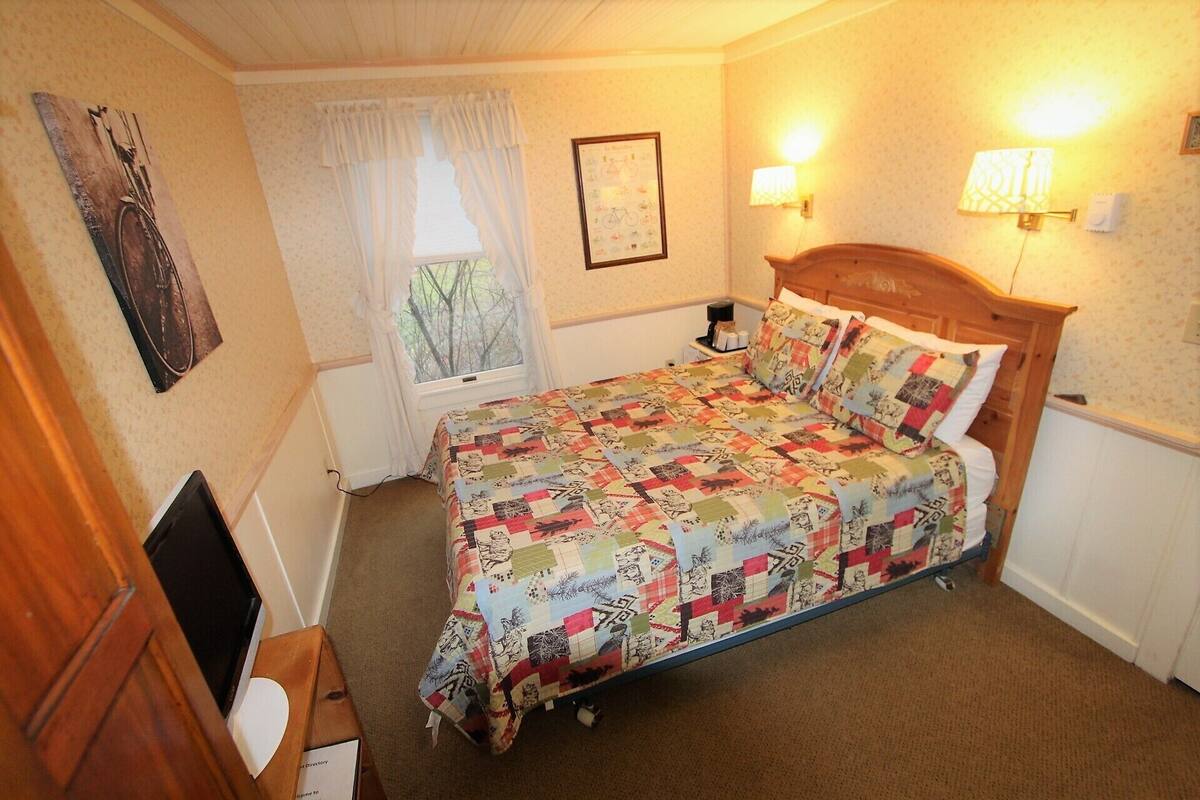 Ein Schlafzimmer mit einem hölzernen Bett, einem Fenster mit Vorhängen, einer Wandleuchte und einem gerahmten Bild.