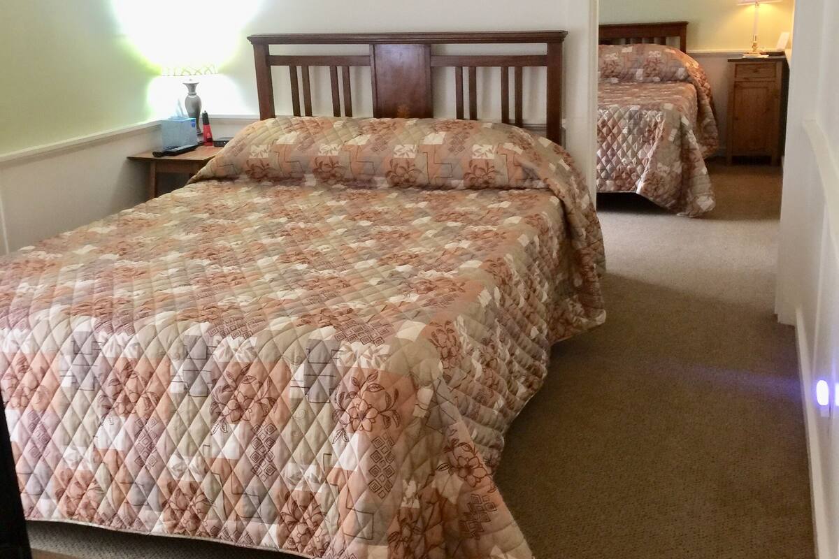 Ein Schlafzimmer mit einem großen Bett, einem Nachttisch, einer Lampe und einem Spiegel.
