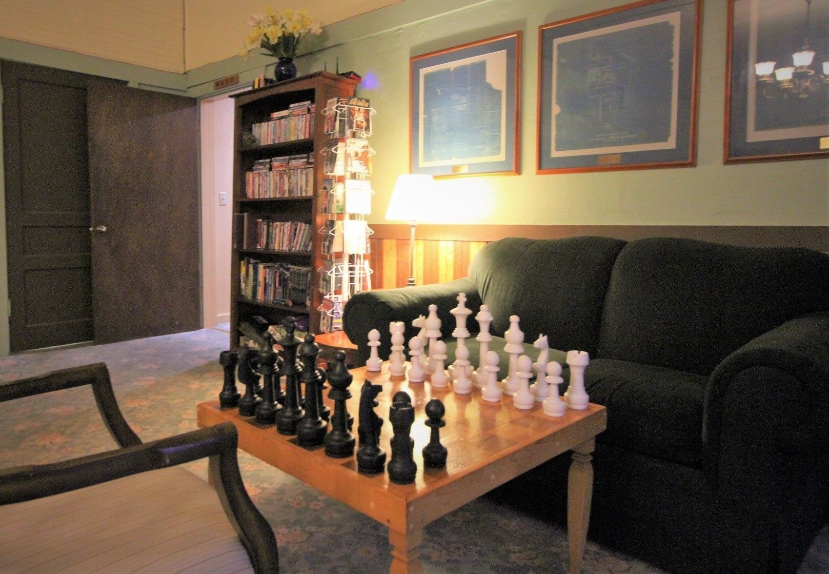 A living room with a chessboard set up on a wooden table, a bookshelf, a lamp, and a couch.