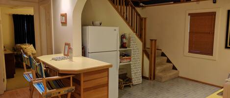 Una cocina compacta con una isla de madera, un refrigerador y una escalera que lleva a un nivel superior.