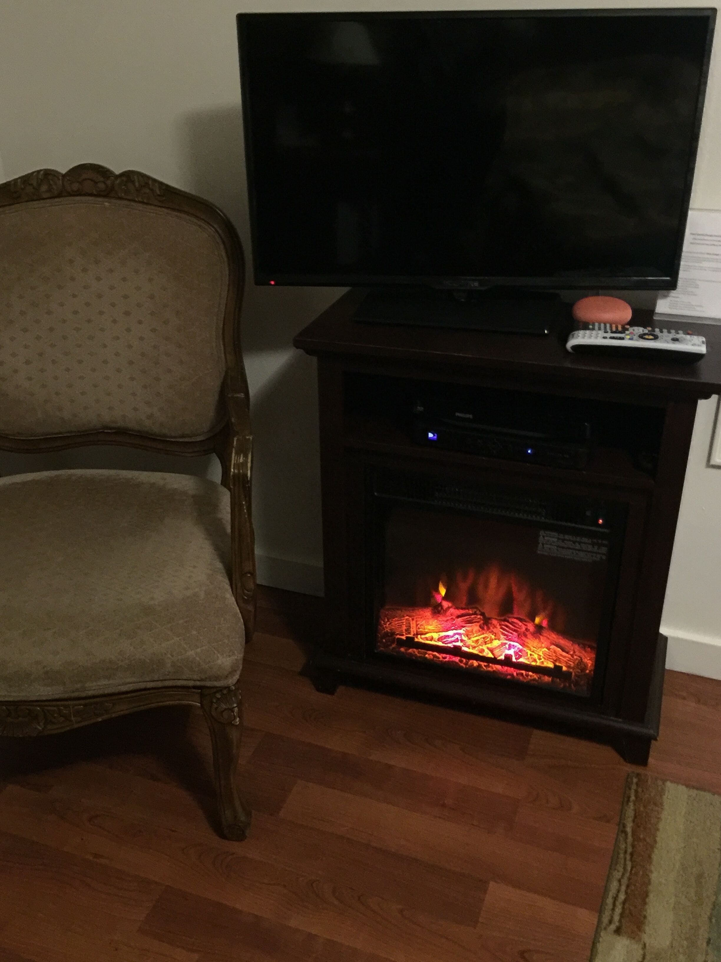 A living room with a television on a stand, a fireplace, and a wooden chair.
