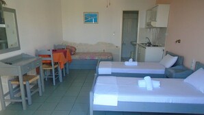 Hotellihuone, jossa on kaksi sänkyä, työpöytä, tuoli, pieni pöytä ja pieni keittiönurkkaus.
