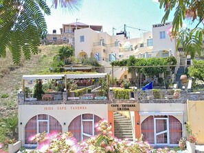 Un edificio de varios pisos con una cafetería y una taberna en la planta baja, con mesas al aire libre y una escalera que lleva a los pisos superiores.