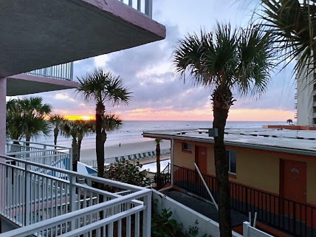A balcony with a view of the beach and palm trees at sunset.