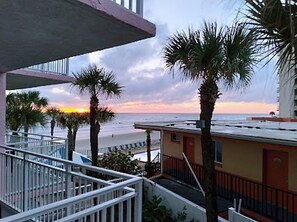 A balcony with a view of the beach and palm trees at sunset. - Flamingo Inn Beachfront (Daytona Beach Shores)