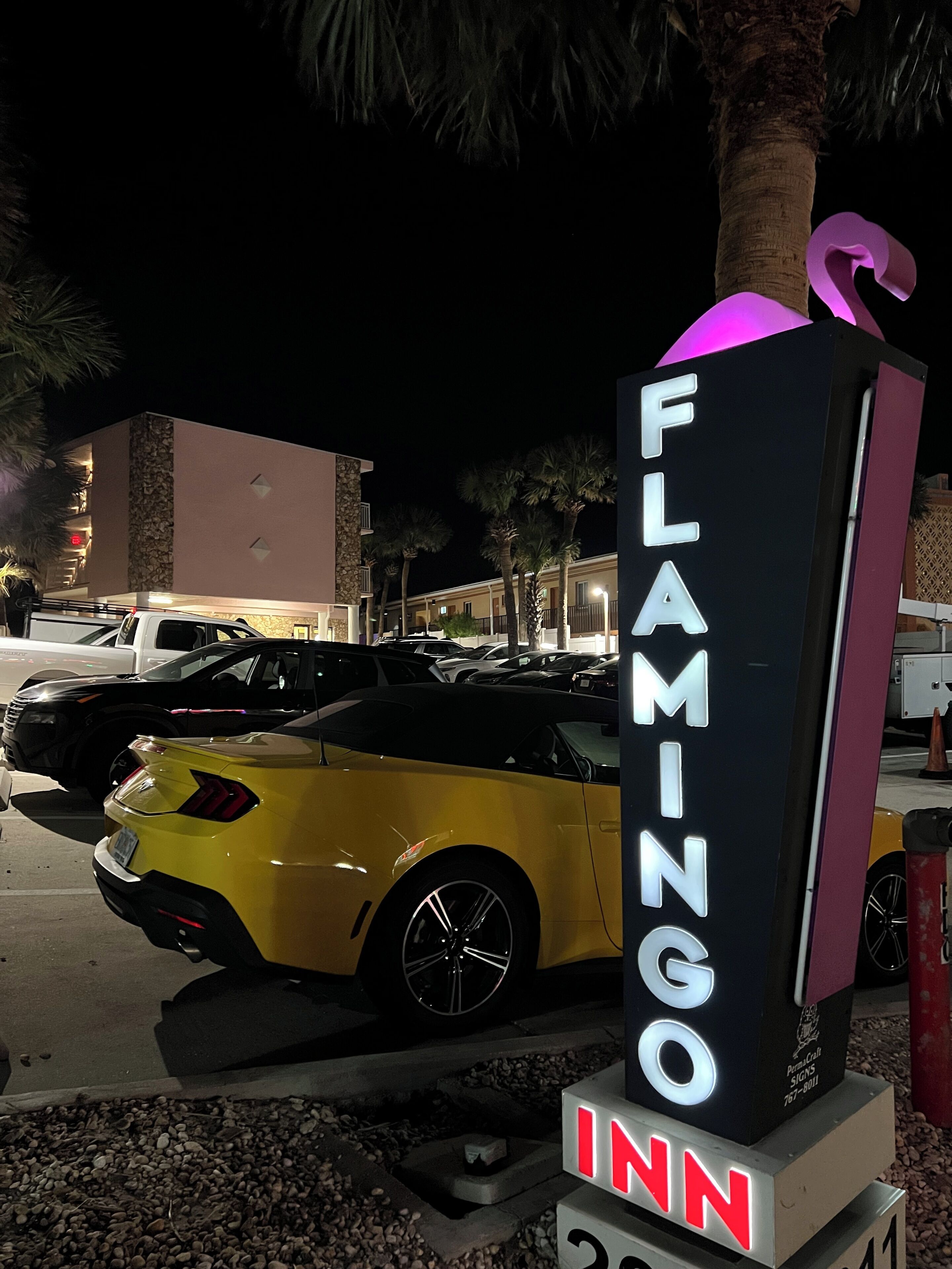 A neon sign for 'FLAMINGO INN' with a yellow convertible car parked nearby.