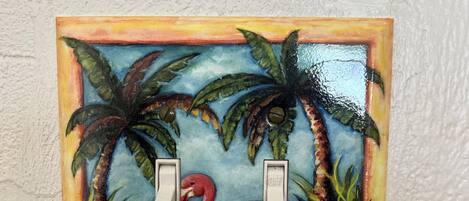 A painting of a pink flamingo with two switches, surrounded by tropical plants and flowers.