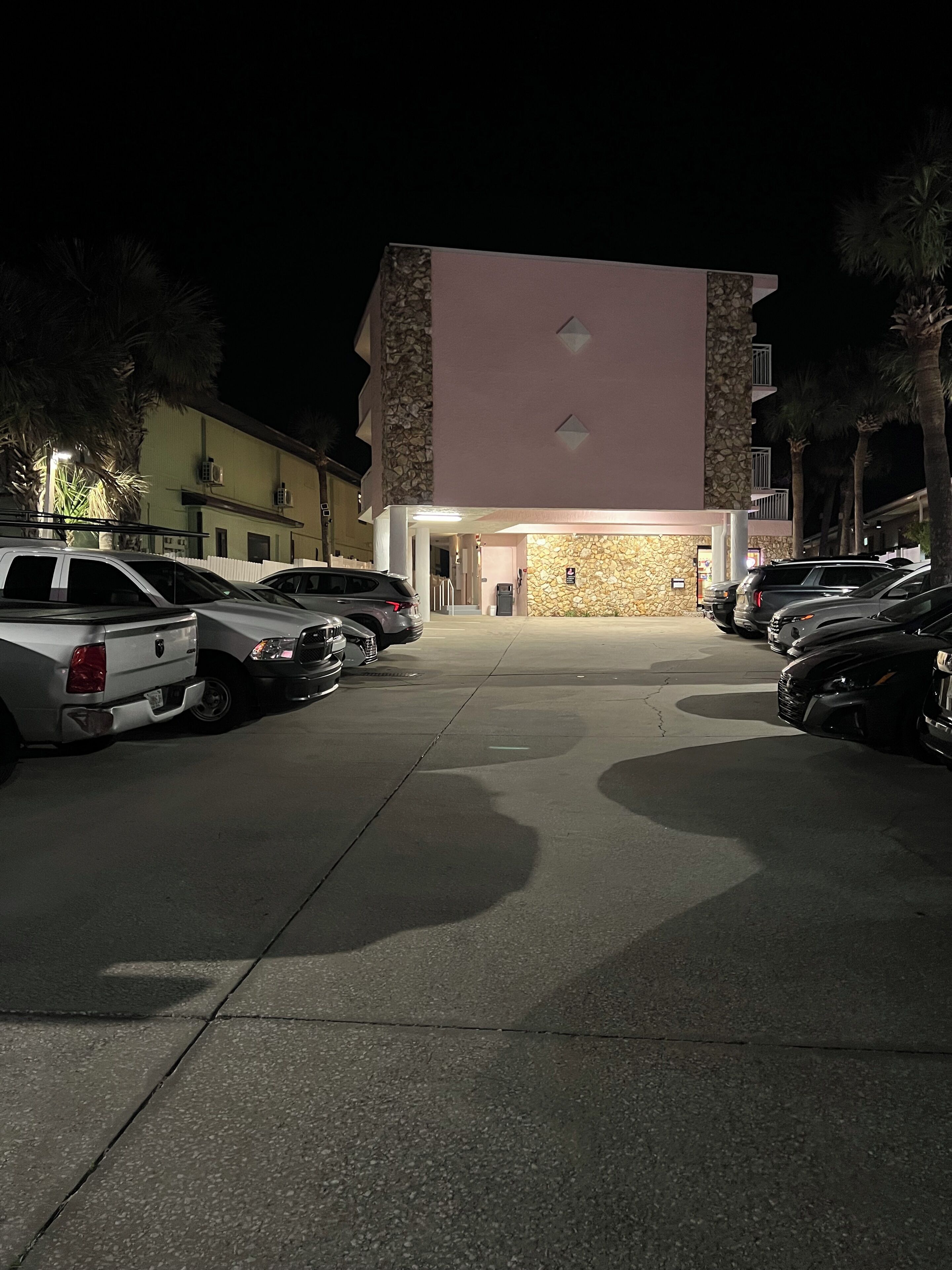 Un parcheggio con diverse auto, un edificio con facciata in pietra e palme.