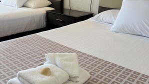 A hotel room with two beds, each with white linens and pillows. There are two wall-mounted lamps on either side of the beds. A painting is visible on the wall above the beds. - Flamingo Inn Beachfront (Daytona Beach Shores)