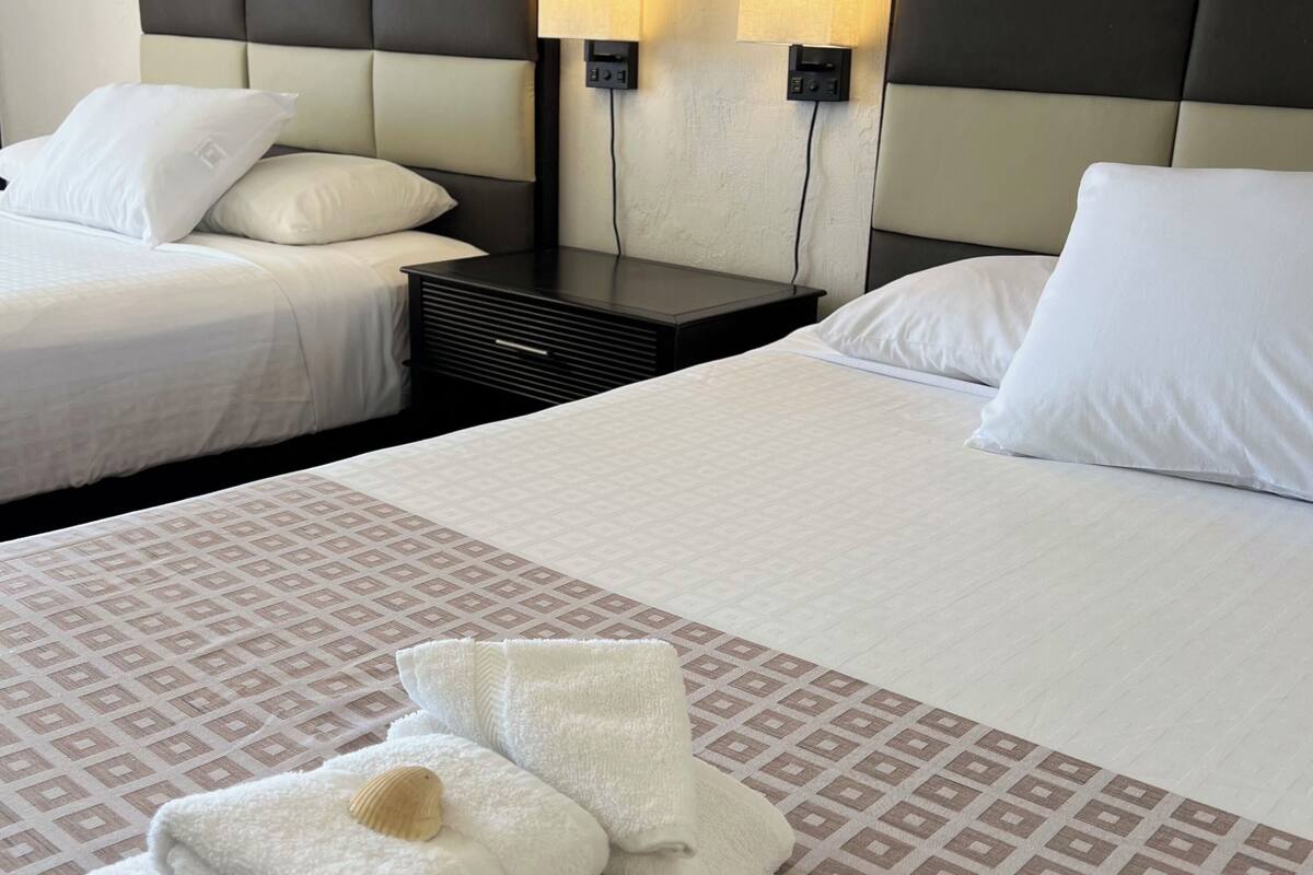 Ein Hotelzimmer mit zwei Betten, jeweils mit weißen Bettwäsche und Kissen. An beiden Seiten der Betten befinden sich Wandlampen. Über den Betten ist ein Gemälde zu sehen.