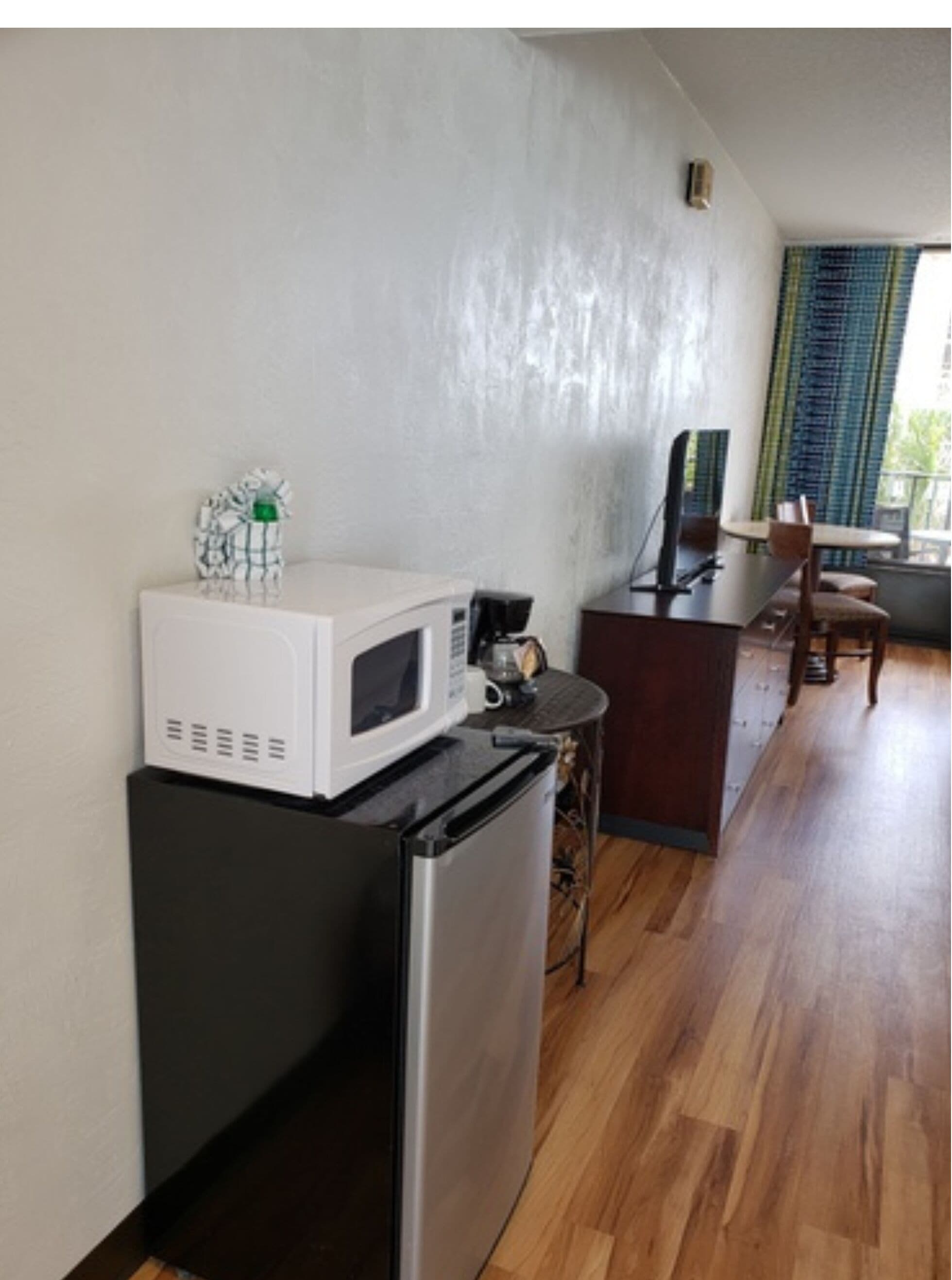 A compact kitchenette with a microwave, refrigerator, and small table with a chair.
