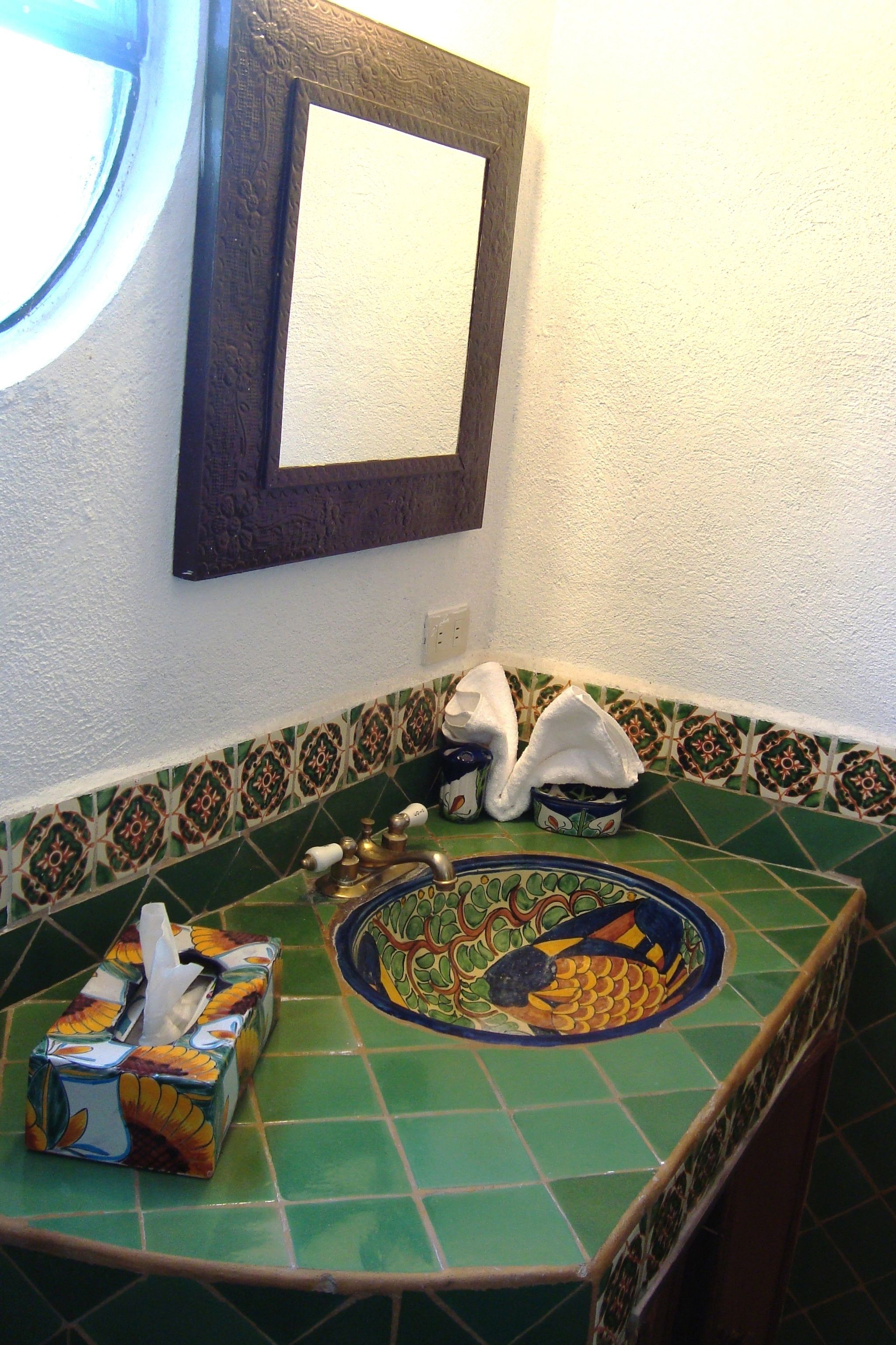 A bathroom with a green tiled floor, a decorative fish bowl, a tissue box, and a mirror on the wall.