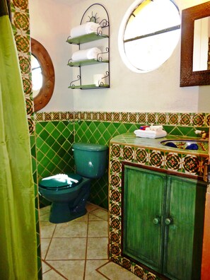 A bathroom with a green toilet, a sink with a decorative cabinet, and a wall-mounted towel rack. - Hospedaje Colibri (San Miguel de Allende)