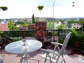 A round glass table with a metal chair on a balcony overlooking a cityscape. - Hospedaje Colibri (San Miguel de Allende)