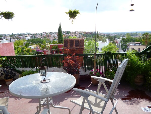 A round glass table with a metal chair on a balcony overlooking a cityscape.