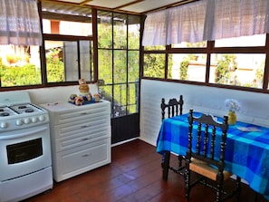 A compact kitchen with a stove, white cabinets, and a dining area with a blue tablecloth and wooden chair. - Hospedaje Colibri (San Miguel de Allende)