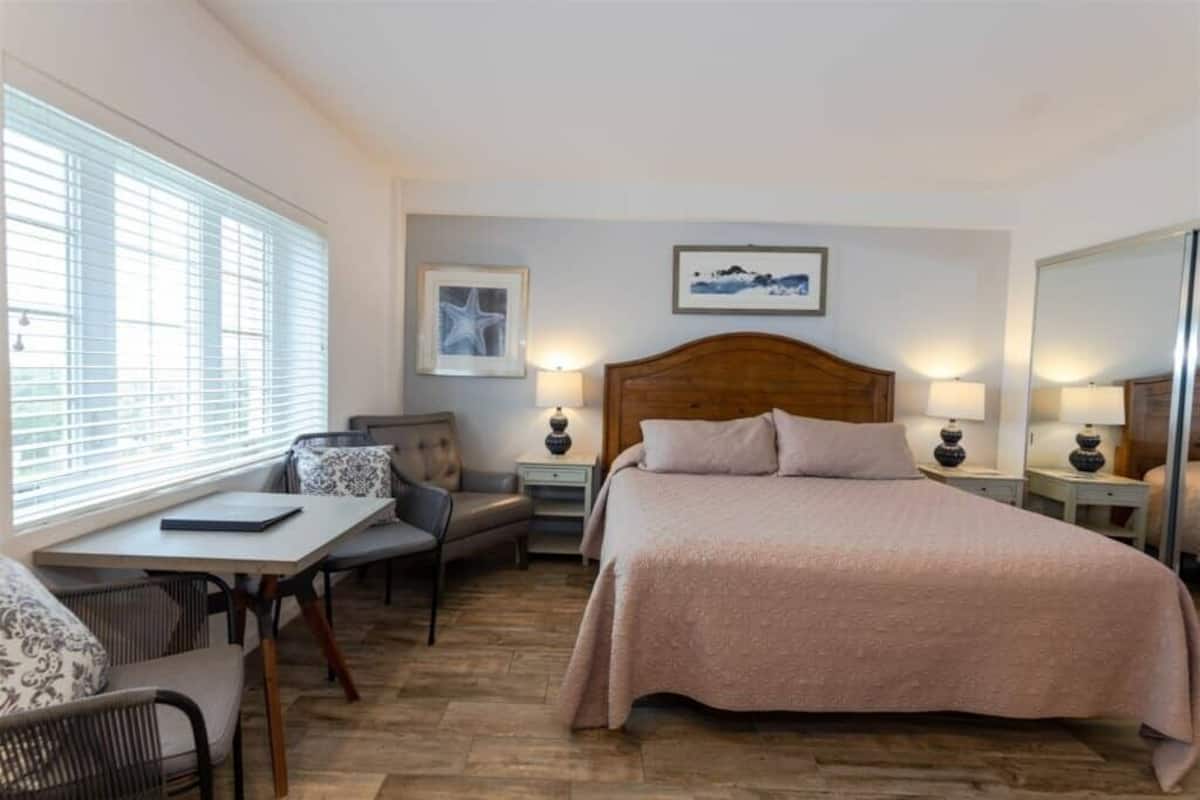 Habitación de hotel con una cama, un escritorio con silla, una mesita y dos mesitas de noche con lámparas.