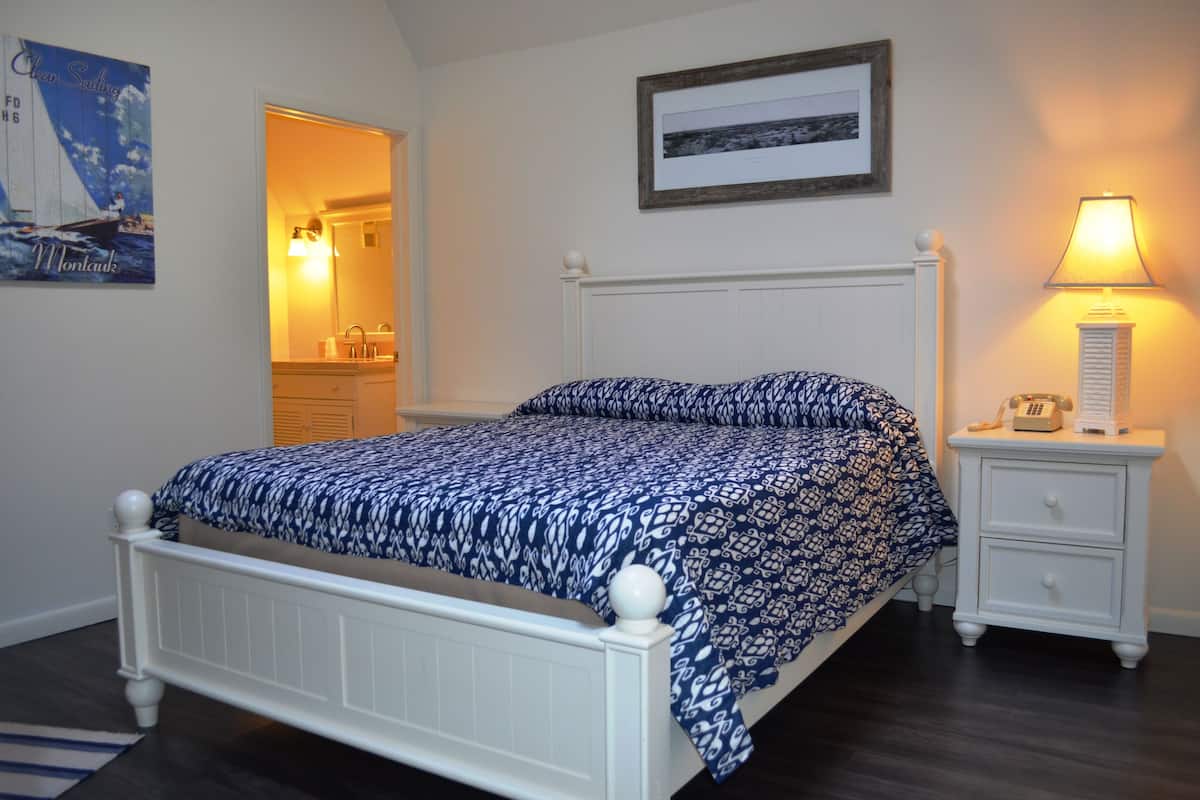 Un dormitorio con una cama, una mesita de noche, una lámpara, un cuadro enmarcado y un espejo.