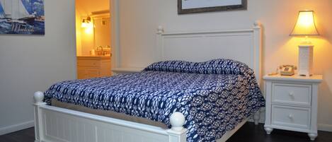 A bedroom with a bed, a nightstand, a lamp, a framed picture, and a mirror.
