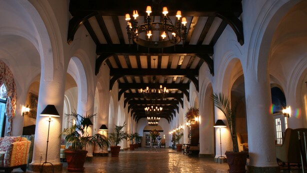 A spacious hallway with high ceilings, arched columns, and chandeliers. - Montauk Manor (Montauk)