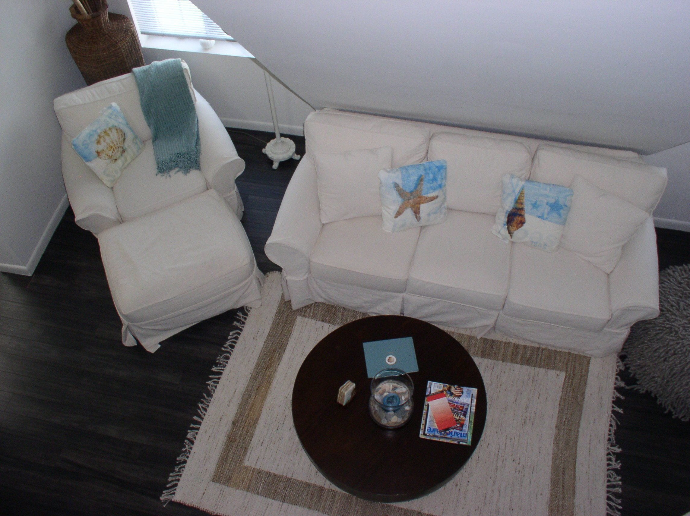 Una sala de estar con un sofá blanco, un sillón blanco y una mesa de centro con revistas y un cuenco pequeño.