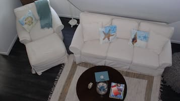 Una sala de estar con un sofá blanco, un sillón blanco y una mesa de centro con revistas y un cuenco pequeño.