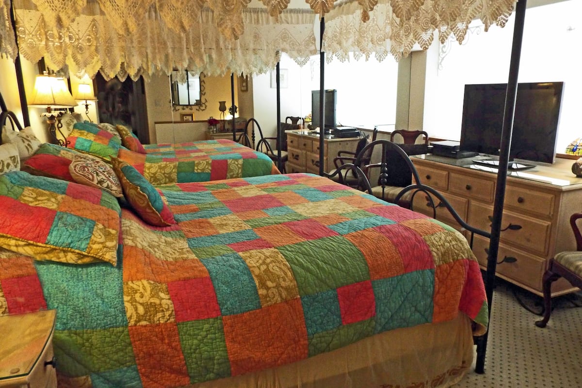 Habitación de hotel con dos camas, un escritorio, una silla y un televisor.