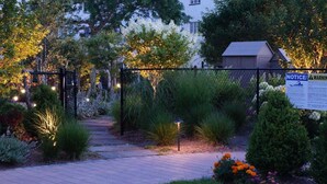 A garden pathway with a fence, illuminated by string lights, leading to a building. - Montauk Manor (Montauk)
