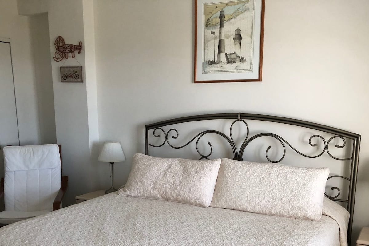 Una cama bien hecha con un edredón blanco texturizado, un cabecero metálico y un cuadro enmarcado en la pared.