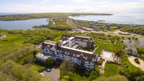 A large, historic building with multiple stories and a prominent tower, surrounded by lush greenery and a body of water. - Montauk Manor (Montauk)