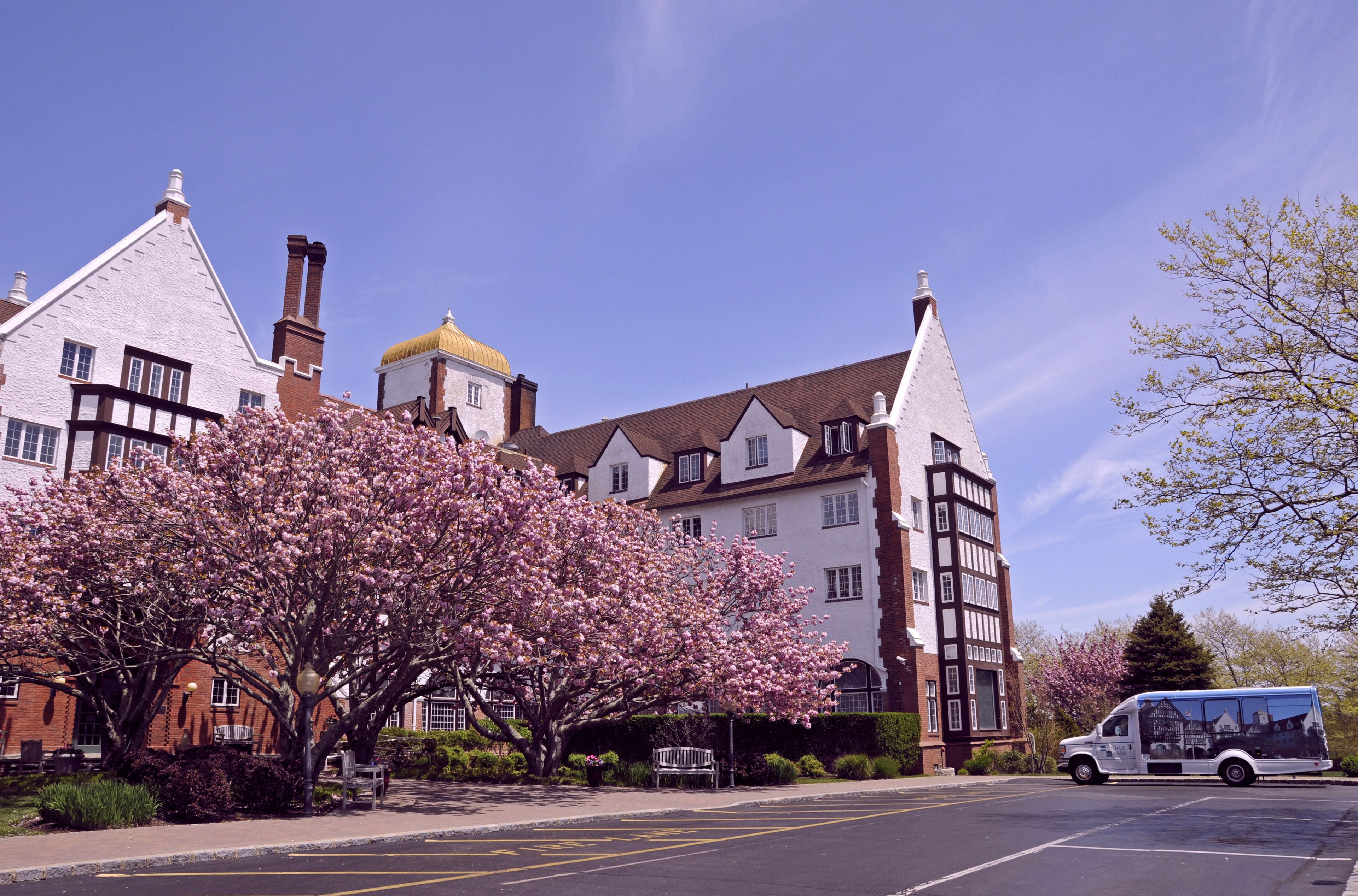 A building with a Tudor-style architecture, including a prominent tower and a large tree with pink blossoms in front.