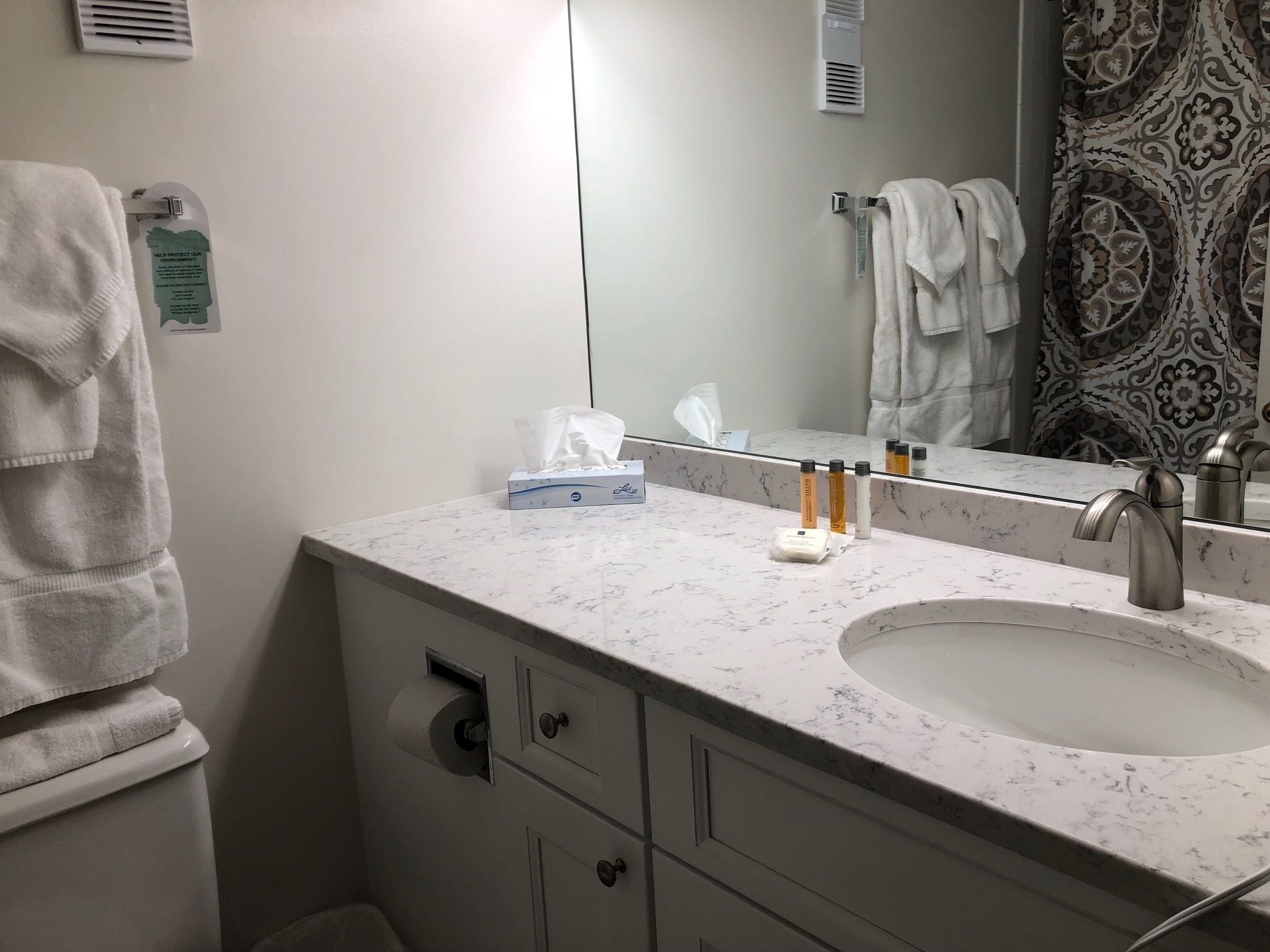 A bathroom with a marble sink, a mirror, a towel rack, and a toilet.