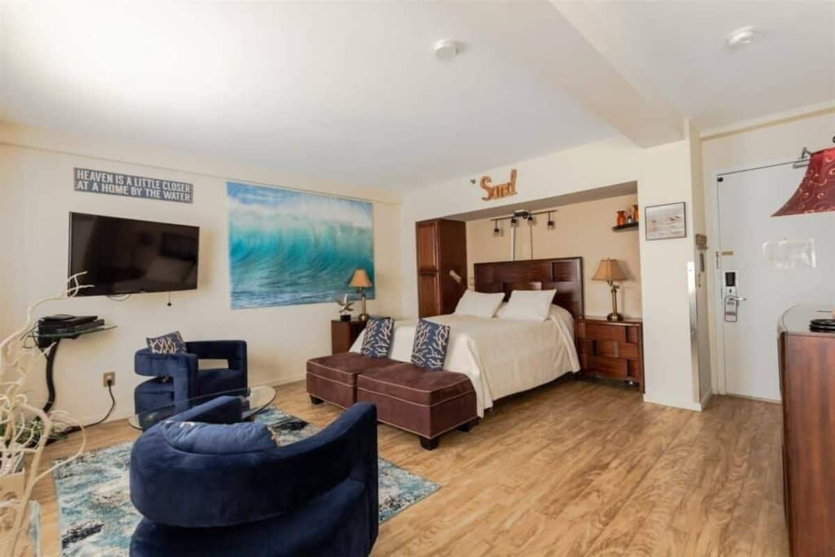 Un dormitorio con cama, televisor, un cuadro y un cartel que dice 'Sea'.