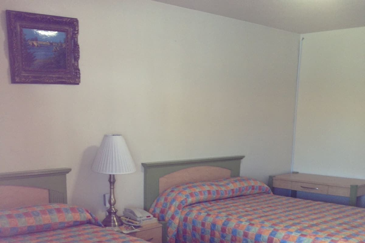 A hotel room with two beds, a nightstand with a lamp, and a small table.
