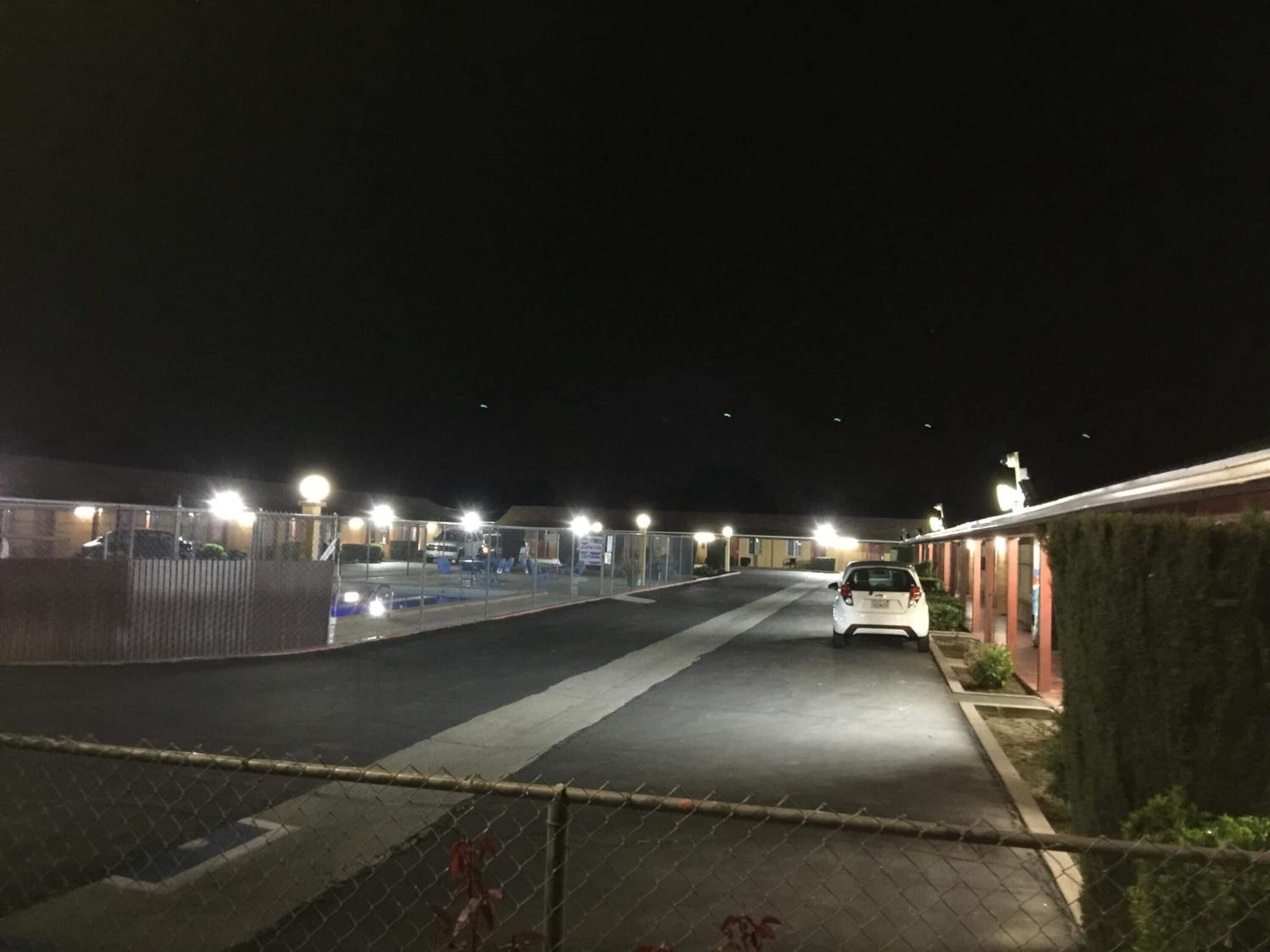 En parkeringsplats avsedd för användning på natten, där en vit bil står parkerad nära en byggnad med ett rött tak.