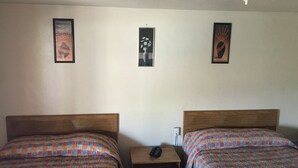 Ein Zimmer mit zwei Betten, einem Nachttisch und drei gerahmten Bildern an der Wand.
