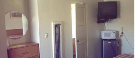 A hotel room with a bed, a dresser, a mirror, a radiator, a television, and a microwave.