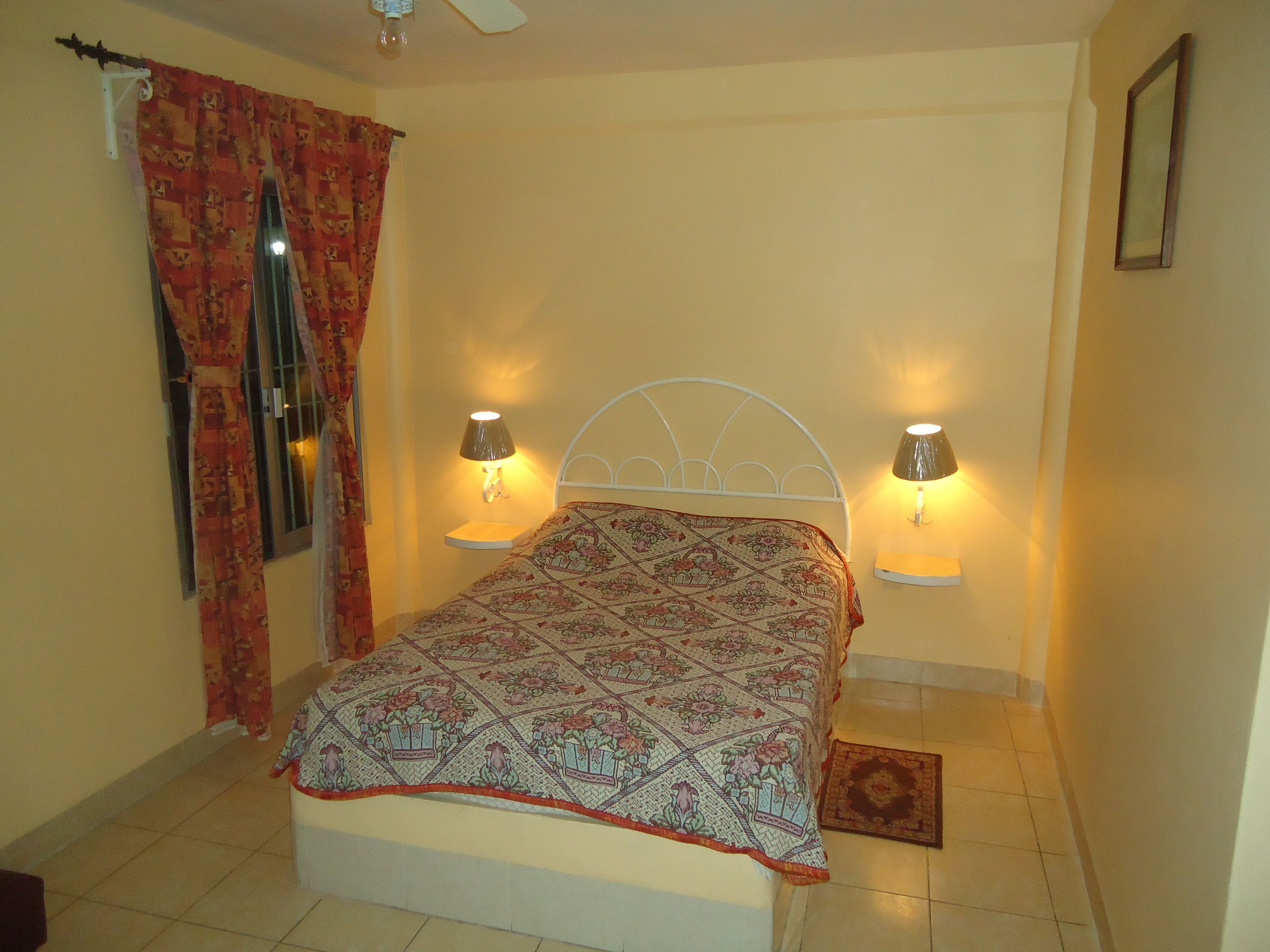 A bedroom with a bed, two bedside lamps, a window with curtains, and a small rug.