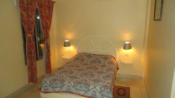 Een slaapkamer met een bed, twee bedlampen, een raam met gordijnen en een kleed.