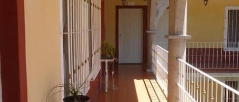 A corridor with a tiled floor, white railings, and a potted plant.