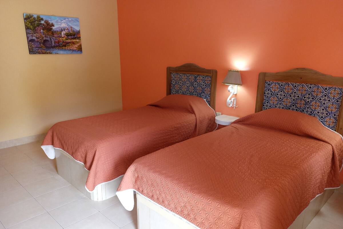 A room with two beds, a small table, and a wall-mounted lamp.