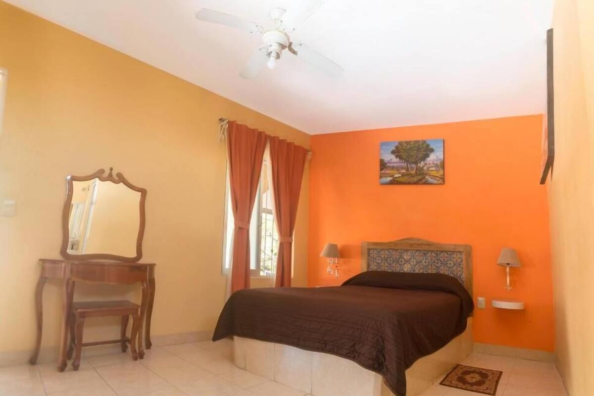 A bedroom with a bed, a ceiling fan, a mirror, and two bedside lamps.