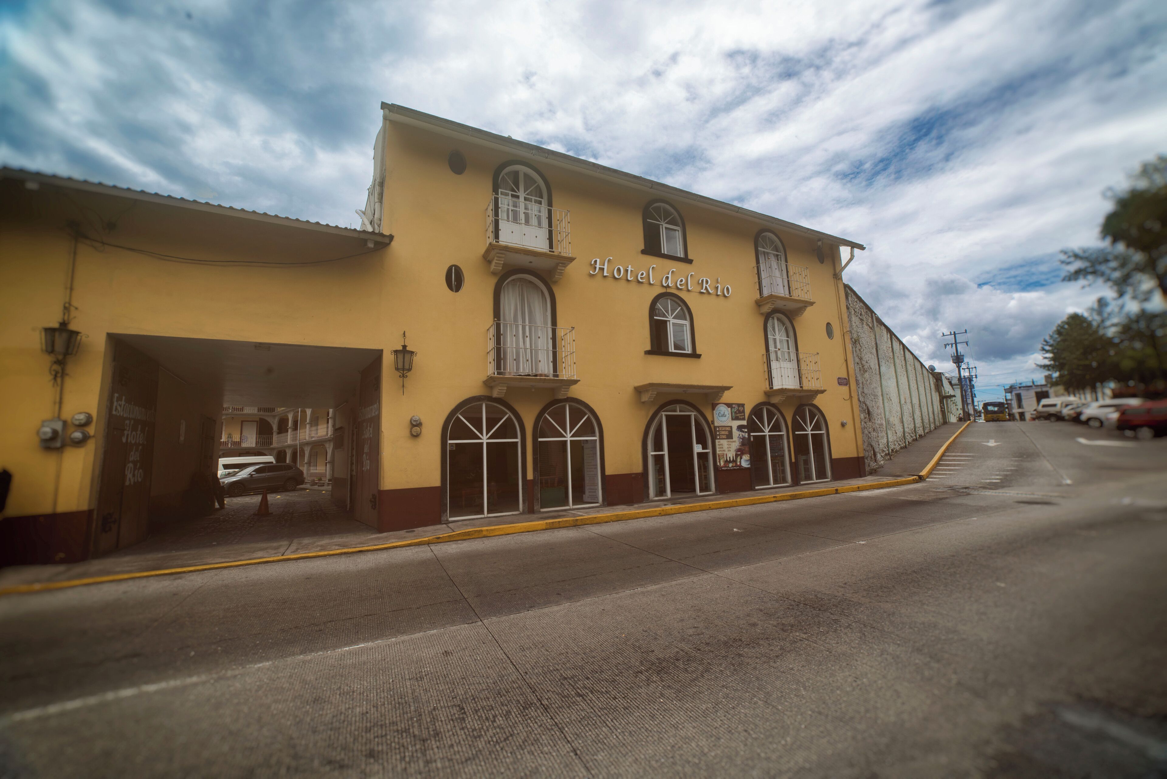 A yellow building with the sign "Hotel del Rio" and multiple windows with balconies.