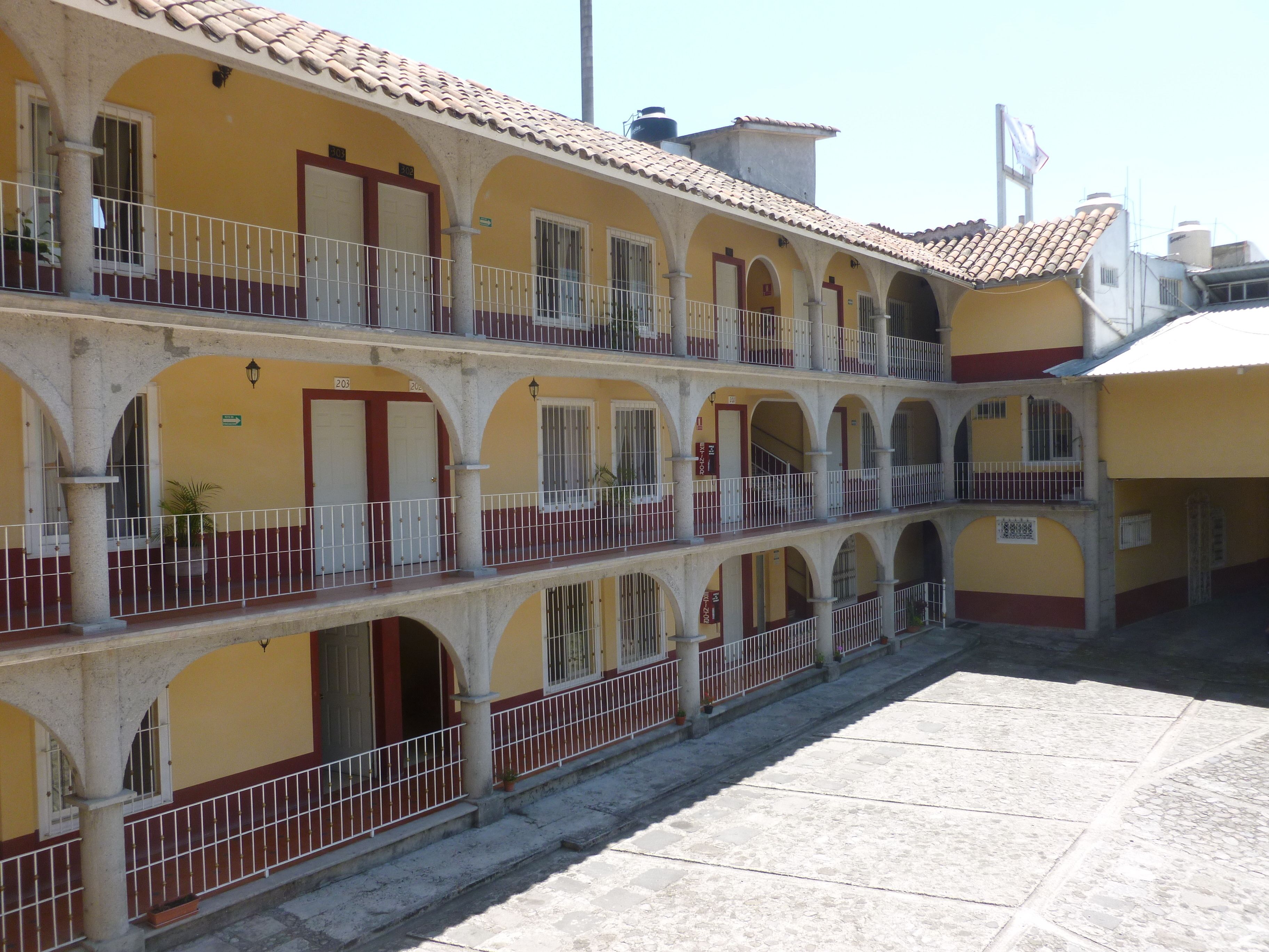 Un immeuble à plusieurs étages, doté d’une façade jaune, de nombreux balcons et d’un toit recouvert de tuiles.