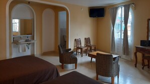 A hotel room with two beds, a dining area with chairs, a television, and a window with curtains.