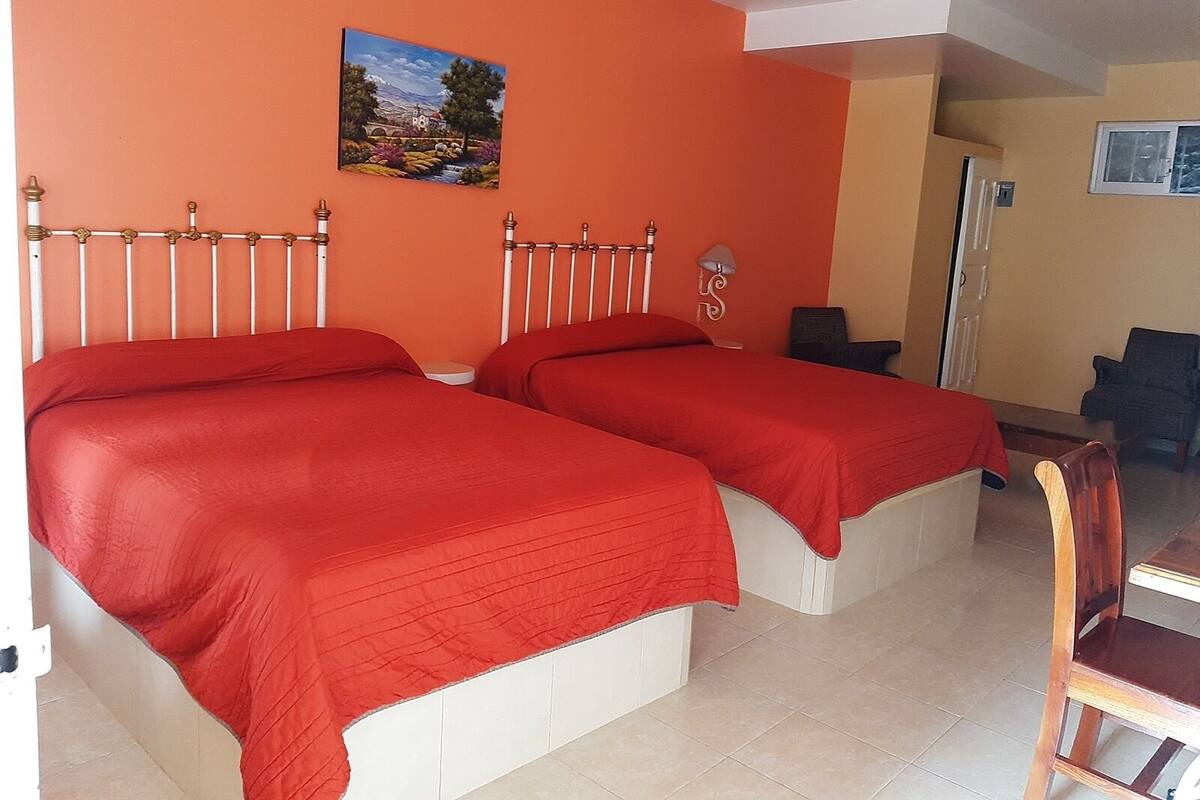 A hotel room with two beds, a painting on the wall, and a chair.