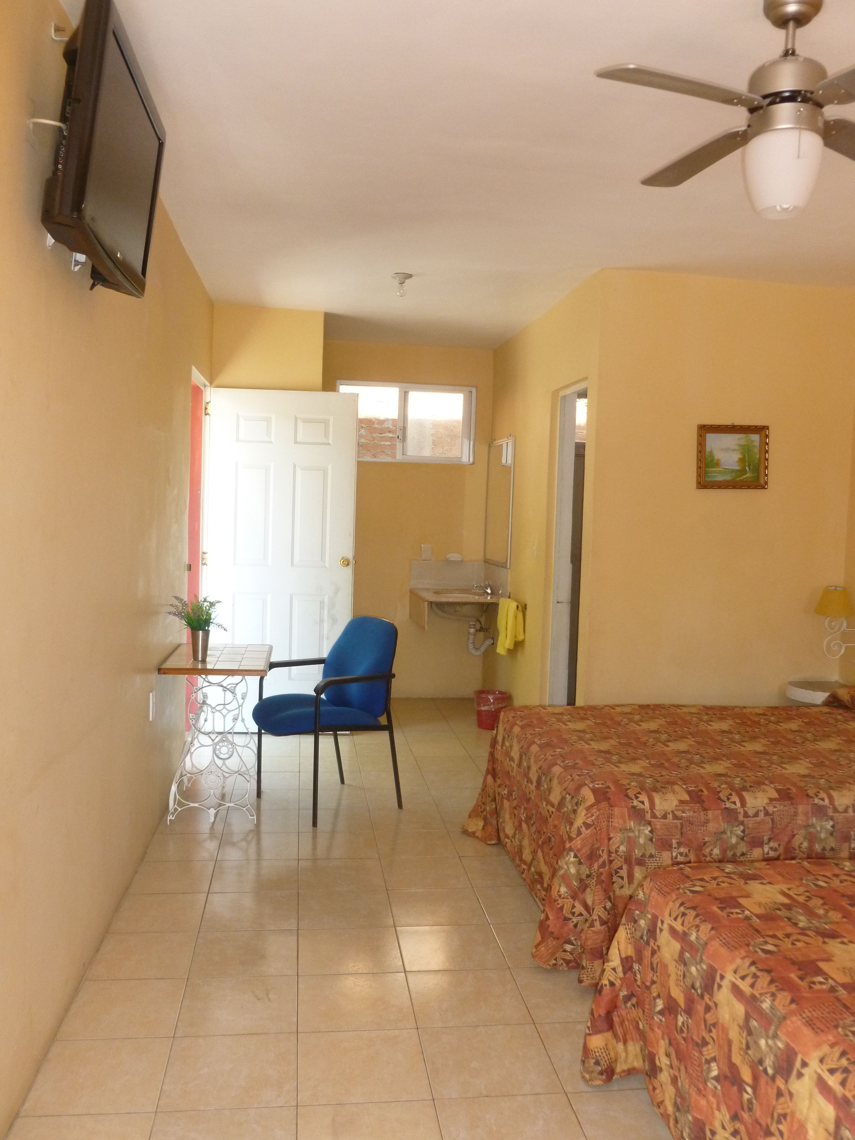 A room with a bed, a chair, a TV, a ceiling fan, and a window.