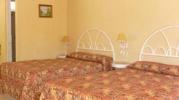 A room with two beds, each with a patterned bedspread, a ceiling fan, and two bedside lamps.