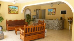 A hotel lobby with a wooden sofa, a stone reception desk, and a tiled floor.