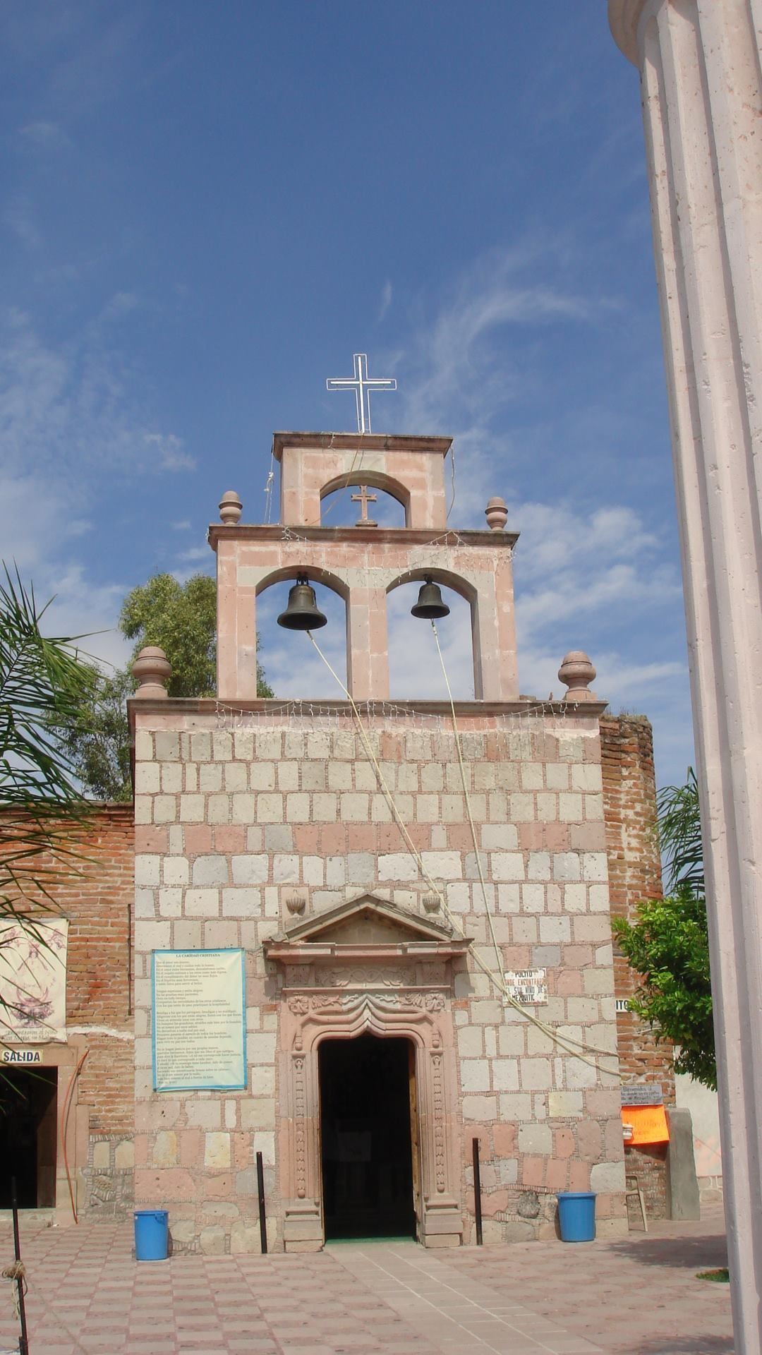 A church with a bell tower, a cross on top, and a sign with text.